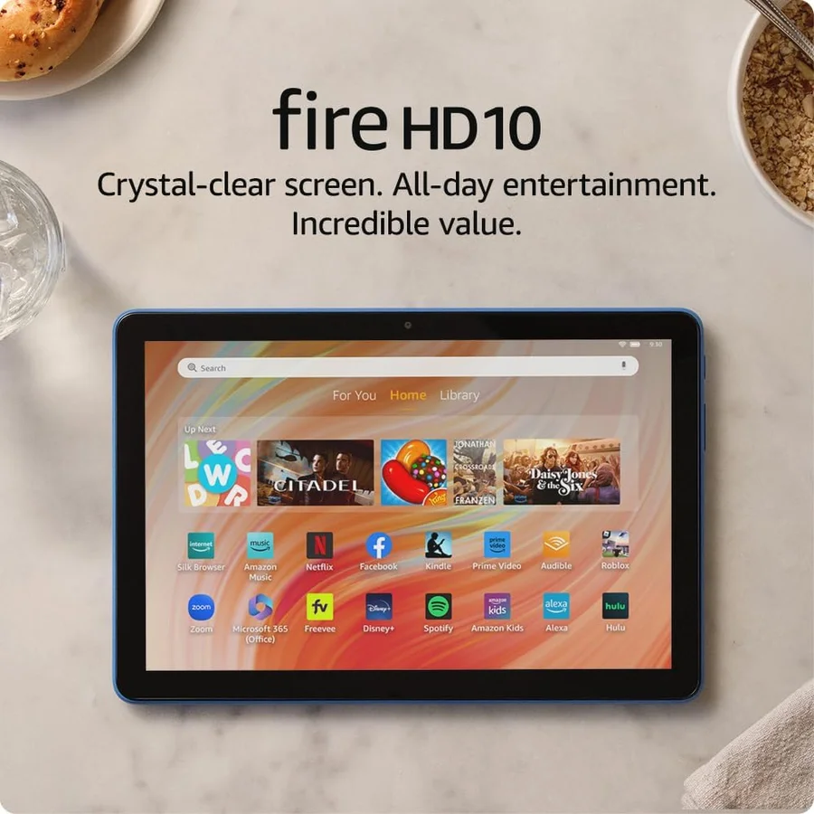 Amazon Fire HD 10 2023 tablet in Lilac color on a couch armrest showing a Prime Video streaming interface, the 10.1-inch Full HD display visible, a cup of coffee on the side table -- the living-room casual streaming scenario