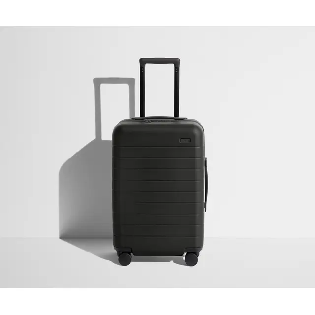 Away The Carry-On polycarbonate hardshell suitcase in matte navy blue, 360-degree spinner wheels, ejectable USB battery panel