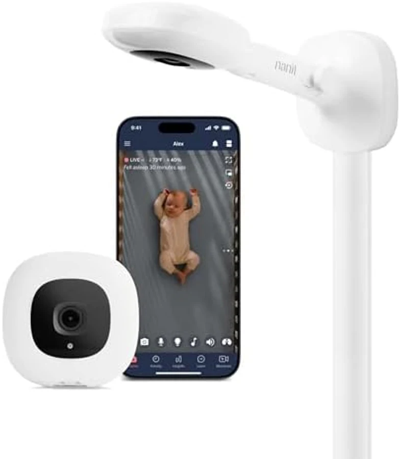 Nanit Pro Smart Baby Monitor system in white with rounded square camera unit, black lens, integrated floor stand mount, paired with a smartphone displaying the Nanit app interface — the 2025 flagship from Nanit, the smartest sleep-tracking baby monitor on the 2026 US market